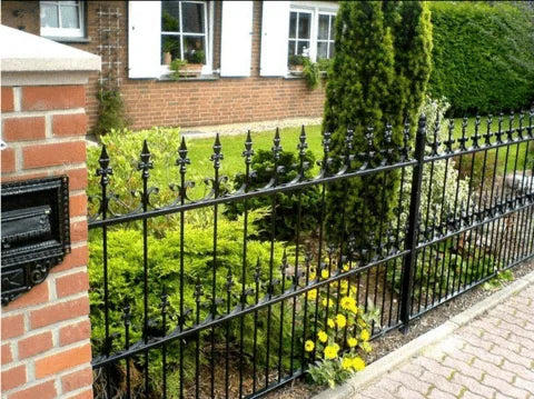 Zwart smeedijzeren hek met sierlijke punten, bakstenen pilaar met brievenbus en tuin bij een woning.